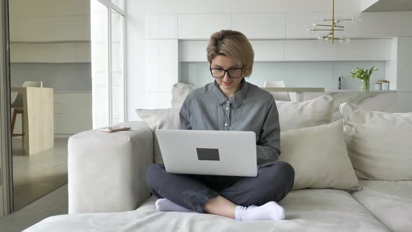 Young Woman Freelancer with Short Fair Hair Types on Laptop