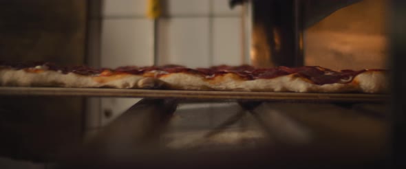 Traditional Al Taglio pepperoni pizza being placed in the hot oven. Slow motion.