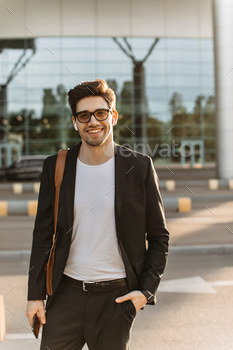 Charming man in black suit, white t-shirt and eyeglasses smiles widely and looks into camera. Brune / Photodune, Misc