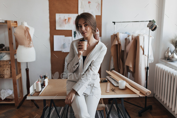 Young lady drinking coffee at her office. Portrait of brunette woman in white pants and shirt enjoy / Photodune, Misc