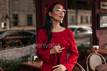 Portrait of cool tanned woman in red beret, elegant dress and eyeglasses holds black handbag and po / Photodune, Misc