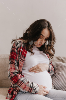 Brunette attractive pregnant woman looks and gently touches belly. Portrait of happy young mother s / Photodune, Misc