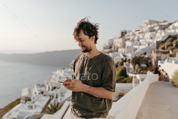 Brunette man in stylish summer outfit chats in phone outside. Guy in dark green t-shirt smiles and / Photodune, Misc