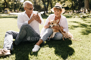Blonde haired woman in hat, striped blouse and jeans holding dog and sitting on grass with man in g / Photodune, Misc