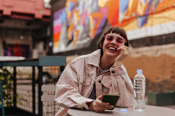 Cheerful woman with brunette hair laughing outside. Modern short-haired girl in bright glasses and / Photodune, Misc