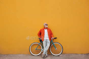 Man in orange jacket and jeans poses with bicycle. Stylish adult with gray beard in sunglasses and / Photodune, Misc