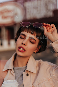 Charming lady with brunette hair posing outdoors. Stylish woman in beige denim jacket and sunglasse / Photodune, Misc