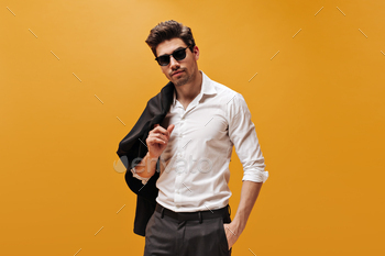 Attractive brunet man in stylish white shirt and trendy sunglasses poses on orange background and h / Photodune, Misc