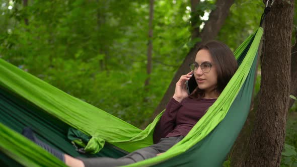 Young Woman in Glasses Talking on the Phone While Lying in a Hammock