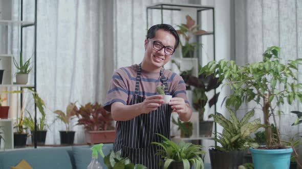 Smiling Asian Man Holding And Showing Cactus Plant To Camera At Home