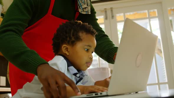 Low angle view of young black father and son using laptop in kitchen of comfortable home 4k