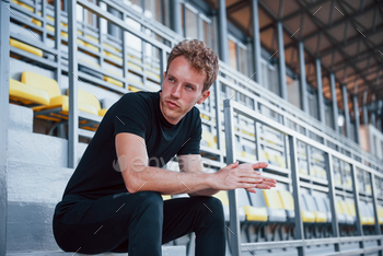 Sits on stairs. Sportive young guy in black shirt and pants outdoors at daytime / Photodune, Misc