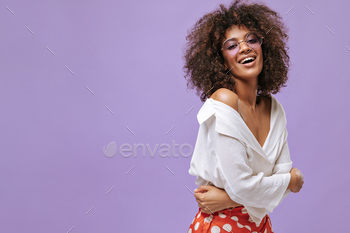 Good-humored girl in light shirt and red trousers laughing on lilac backdrop. Curly woman in eyegla / Photodune, Misc