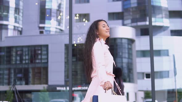 A Girl in a Dress After Shopping with Packages in Her Hands is Happy with the Purchases