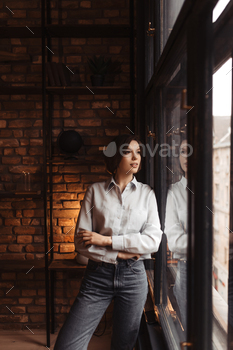 Beautiful woman in blue shirt and jeans looks outside window. Attractive lady in stylish denim pant / Photodune, Misc