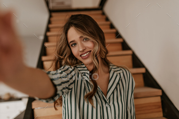 Tanned blue-eyed woman in striped silk green and white shirt smiles sincerely and takes selfie at h / Photodune, Misc