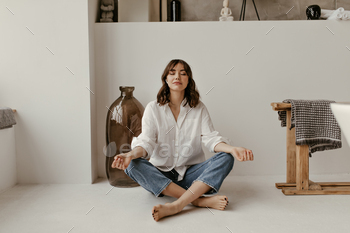 Young brunette woman in jeans and white stylish shirt sits on floor in bathroom. Calm curly lady in / Photodune, Misc
