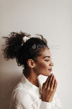Profile portrait of brunette curly woman puts hands together. Dark-skinned lady on white blouse smi / Photodune, Misc
