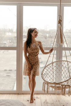Happy calm Asian brunette woman in stylish beige polka dot dress smiles sincerely, poses near windo / Photodune, Misc