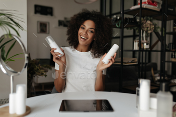 Attractive healthy woman holds two white face cream bottles and smiles. Brunette dark-skinned lady / Photodune, Misc