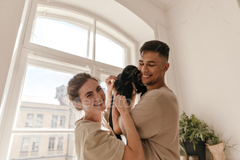 Young family with black puppy having fun in light room. Pretty lady with beige t-shirt and brunette / Photodune, Misc