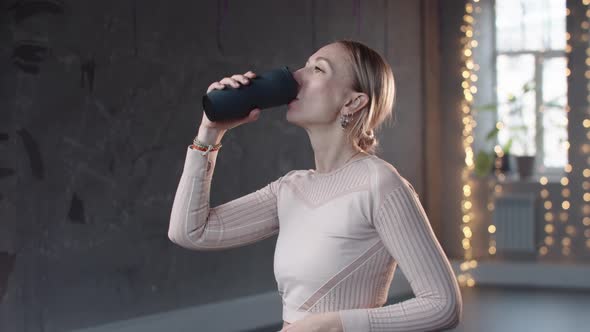 A Woman in a White Sweater Drinks Water in the Studio