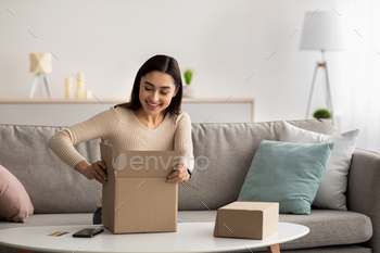 Happy arabian woman sitting on couch at home, opening carton box, received parcel from shop / Photodune, Misc