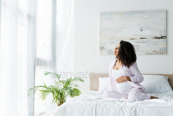 happy young pregnant african american woman sitting on bed and touching belly / Photodune, Misc