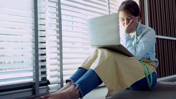 Stressed Asian entrepreneur sitting beside the window because her shop has stopped doing business.