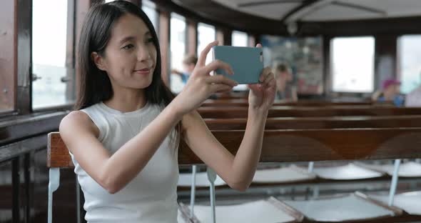 Woman taking photo on cellphone inside ferry at Hong Kong city 