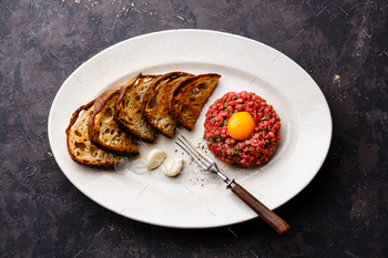 Beef tartare with pickled cucumber and toasts on white plate on dark background / Photodune, Misc