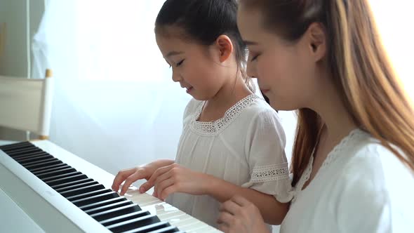 Asian mother watching young daughter play keyboard at home