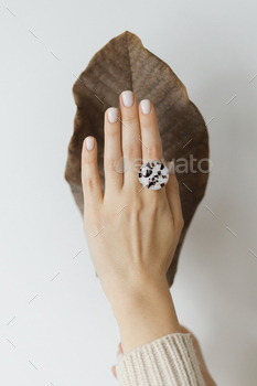 Stylish modern round ring on beautiful hand on background of brown dried big leaf on white wall / Photodune, Misc