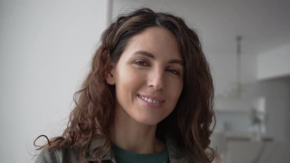 Young Woman with Curly Hair Smiles Looking Into Camera