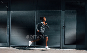 Side view of young african american woman in sportive clothes that runs near wall / Photodune, Misc