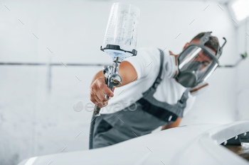 Uses painting gun. Caucasian automobile repairman in uniform works in garage / Photodune, Misc