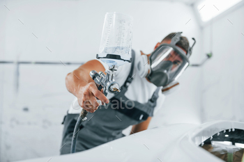 Uses painting gun. Caucasian automobile repairman in uniform works in garage / Photodune, Misc