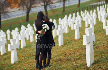 Two young women in black clothes visiting cemetery with many white crosses / Photodune, Misc