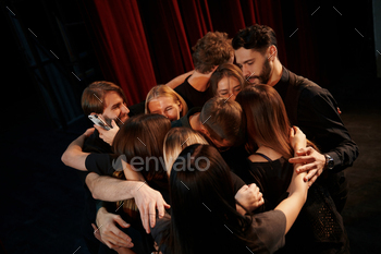 Embracing each other. Group of actors in dark colored clothes on rehearsal in the theater / Photodune, Misc