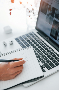 Using laptop and notepad. Young female freelancer working indoors in the office at daytime / Photodune, Misc
