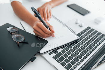 Using laptop and notepad. Young female freelancer working indoors in the office at daytime / Photodune, Misc