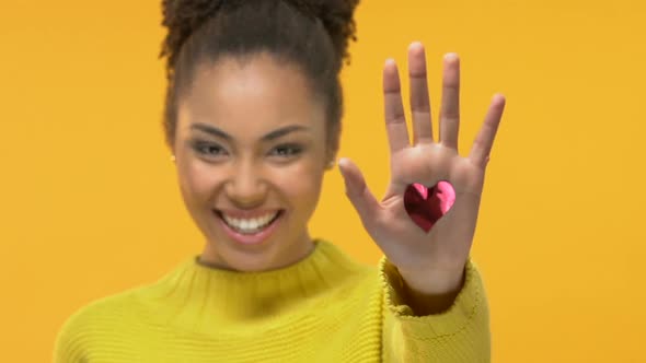 Cheerful Black Female Showing Red Heart in Hand on Yellow Background, Holiday