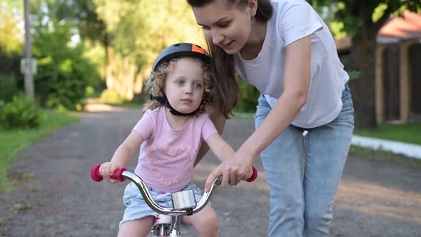 mother teaches her daughter to ride a bike. Little girl in helmet learns to ride