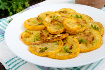 Fried zucchini slices on a white plate on a dark wooden background. / Photodune, Misc