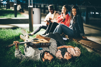 Multiracial young people playing guitar and singing on street at the night city. / Photodune, Misc