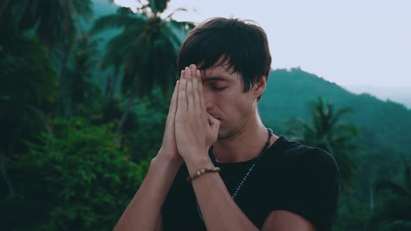 Religious Young Man Holding Hands in Namaste Gesture Standing on Beautiful Jungle Nature with Eyes