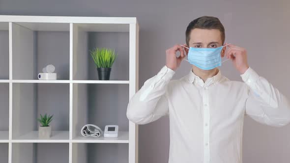 Young Doctor Puts a Protective Mask on His Face in a Cozy Office and Looks at the Camera