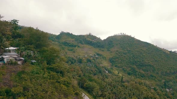 Aerial flying close to a mountainside with houses on it and covered by lush forest in central Cebu