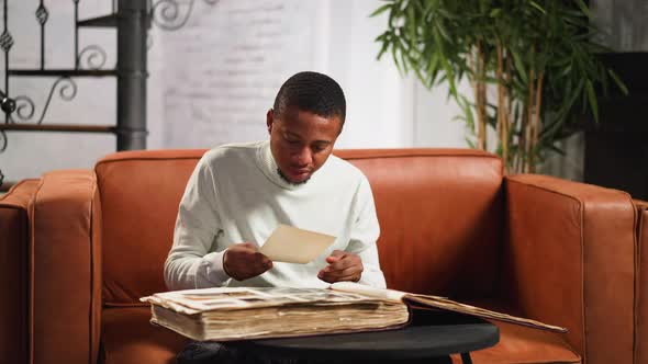 Emotional AfricanAmerican Man Looks at Old Picture at Home