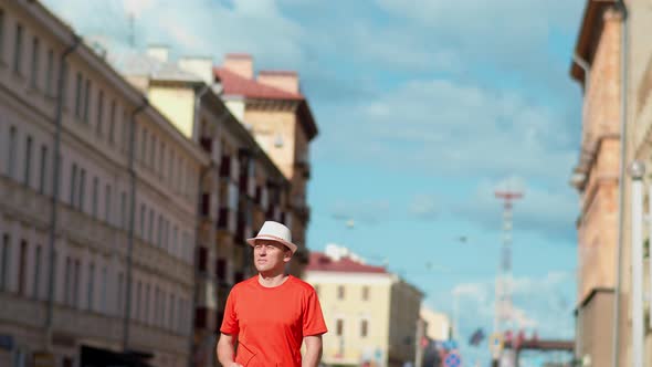 Young Male Tourist in White Hat Walks Along City Street Camera Tracking